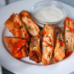 seven buffalo chicken egg rolls on a plate with ranch on the side.