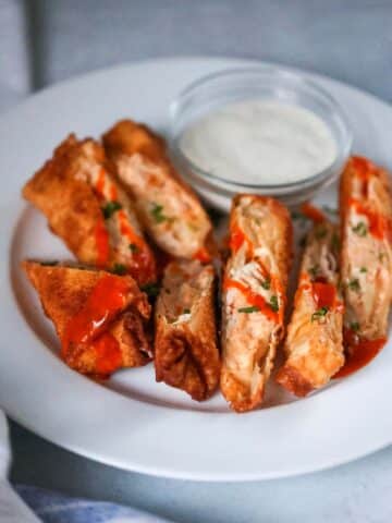 seven buffalo chicken egg rolls on a plate with ranch on the side.