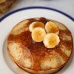 A stack of banana oatmeal pancakes with sliced bananas and maple syrup on top.