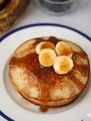 A stack of banana oatmeal pancakes with sliced bananas and maple syrup on top.