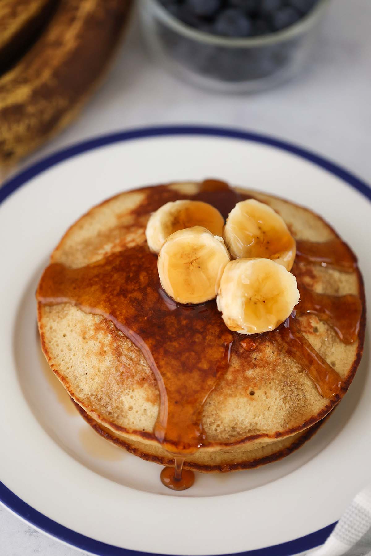 A stack of banana oatmeal pancakes with sliced bananas and maple syrup on top. 