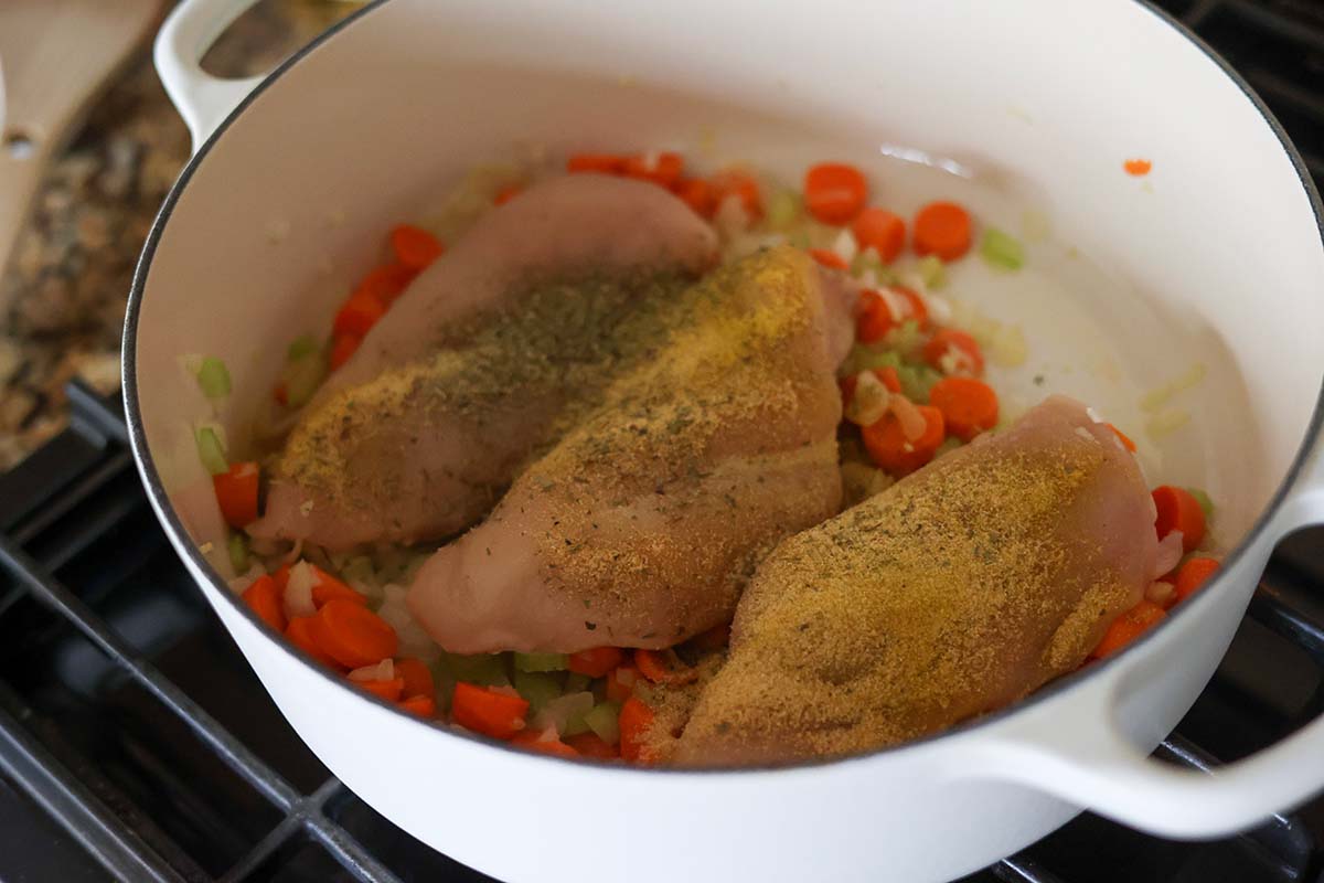 three raw chicken breasts and veggies in a pot. 