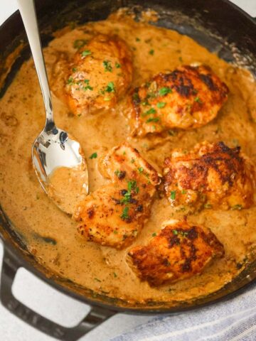 creamy spicy chicken thighs in a skillet with a spoon.