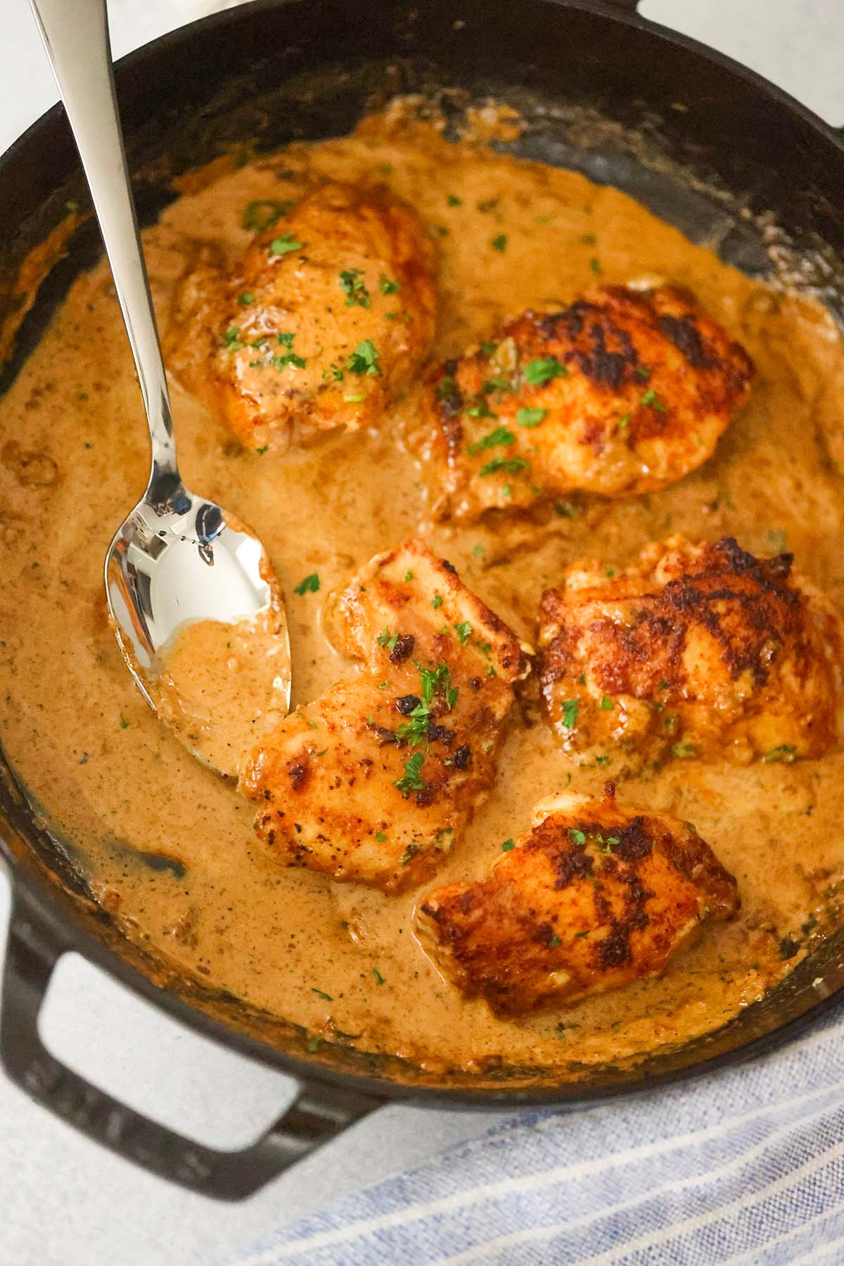 creamy spicy chicken thighs in a skillet with a spoon. 
