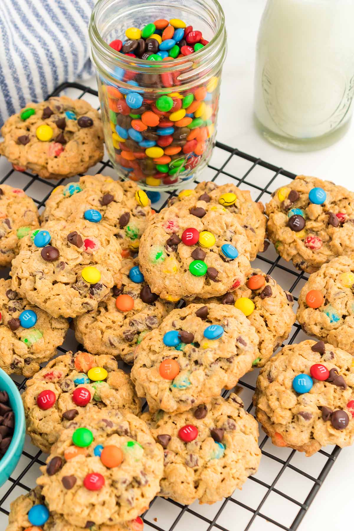 monster cookies on a wire rack with milk and m&ms on the side. 