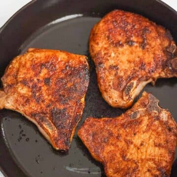 three bone-in pan seared pork chops in a cast iron skillet.