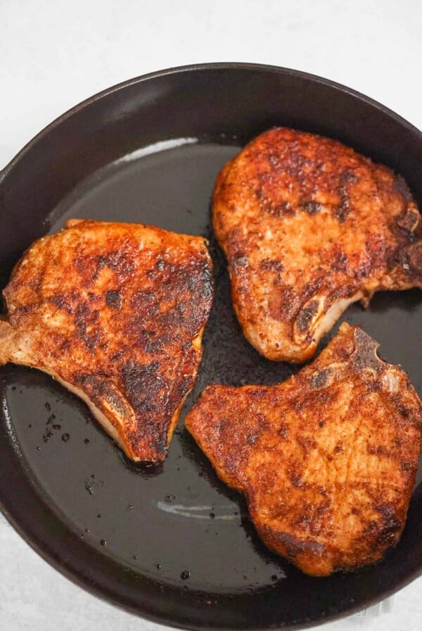 three bone-in pan seared pork chops in a cast iron skillet.