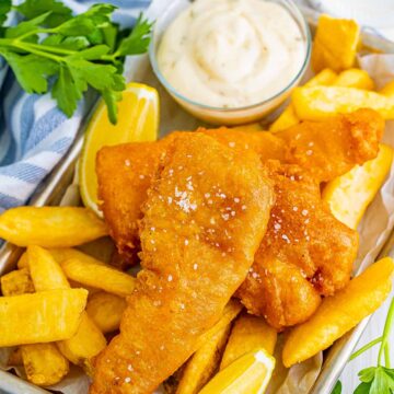 beer battered cod fish with chips, lemon wedges, salt, and tartar sauce.