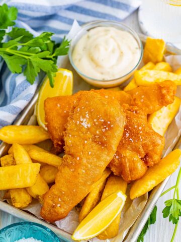 beer battered cod fish with chips, lemon wedges, salt, and tartar sauce.