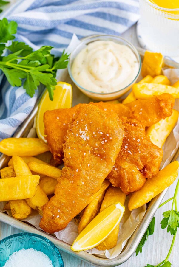 beer battered cod fish with chips, lemon wedges, salt, and tartar sauce.