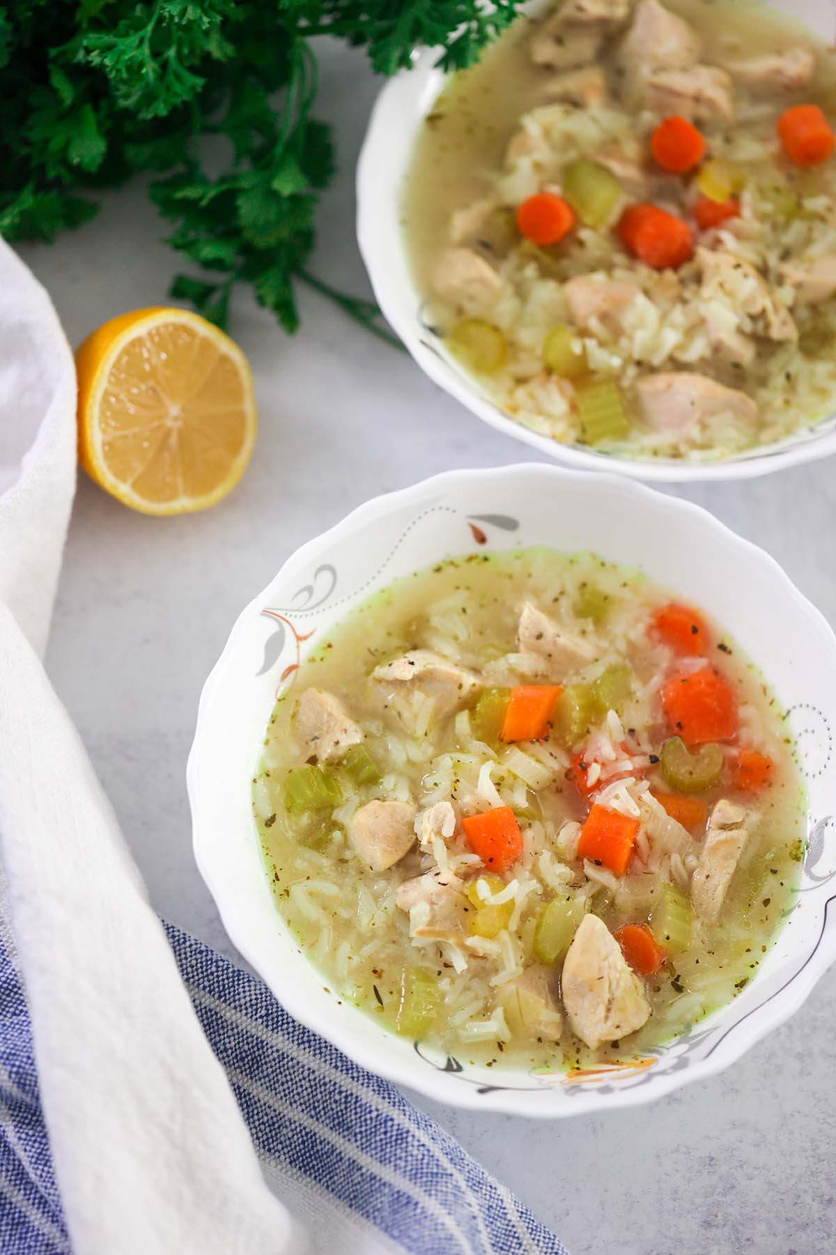 two bowls of chicken and rice soup with lemon and parsley on the side. 