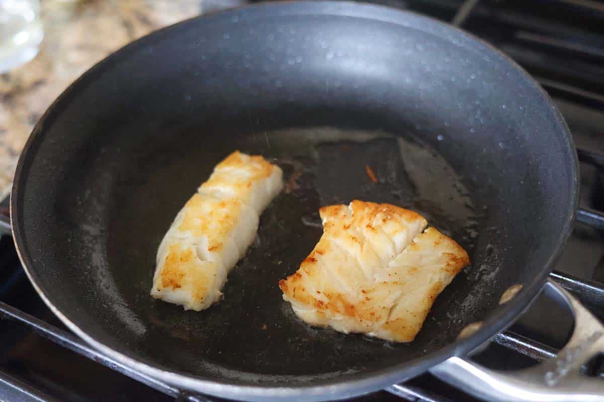 two cod fillets cooking in a skillet. 
