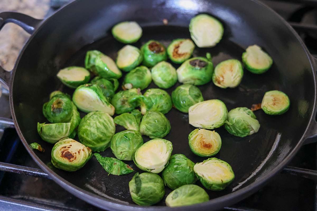 Brussels sprouts pan searing in a skillet on the stovetop. 