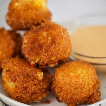 hush puppies on a small plate with sauce on the side.