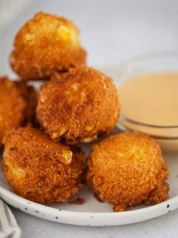 hush puppies on a small plate with sauce on the side.