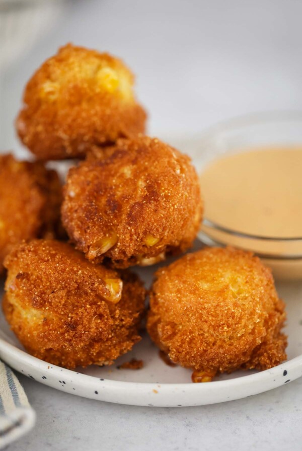 hush puppies on a small plate with sauce on the side.