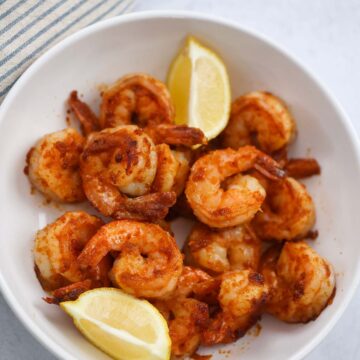 Pan seared shrimp in a bowl with lemon wedges on the side.