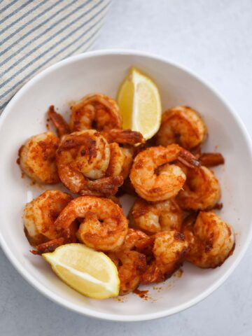 Pan seared shrimp in a bowl with lemon wedges on the side.