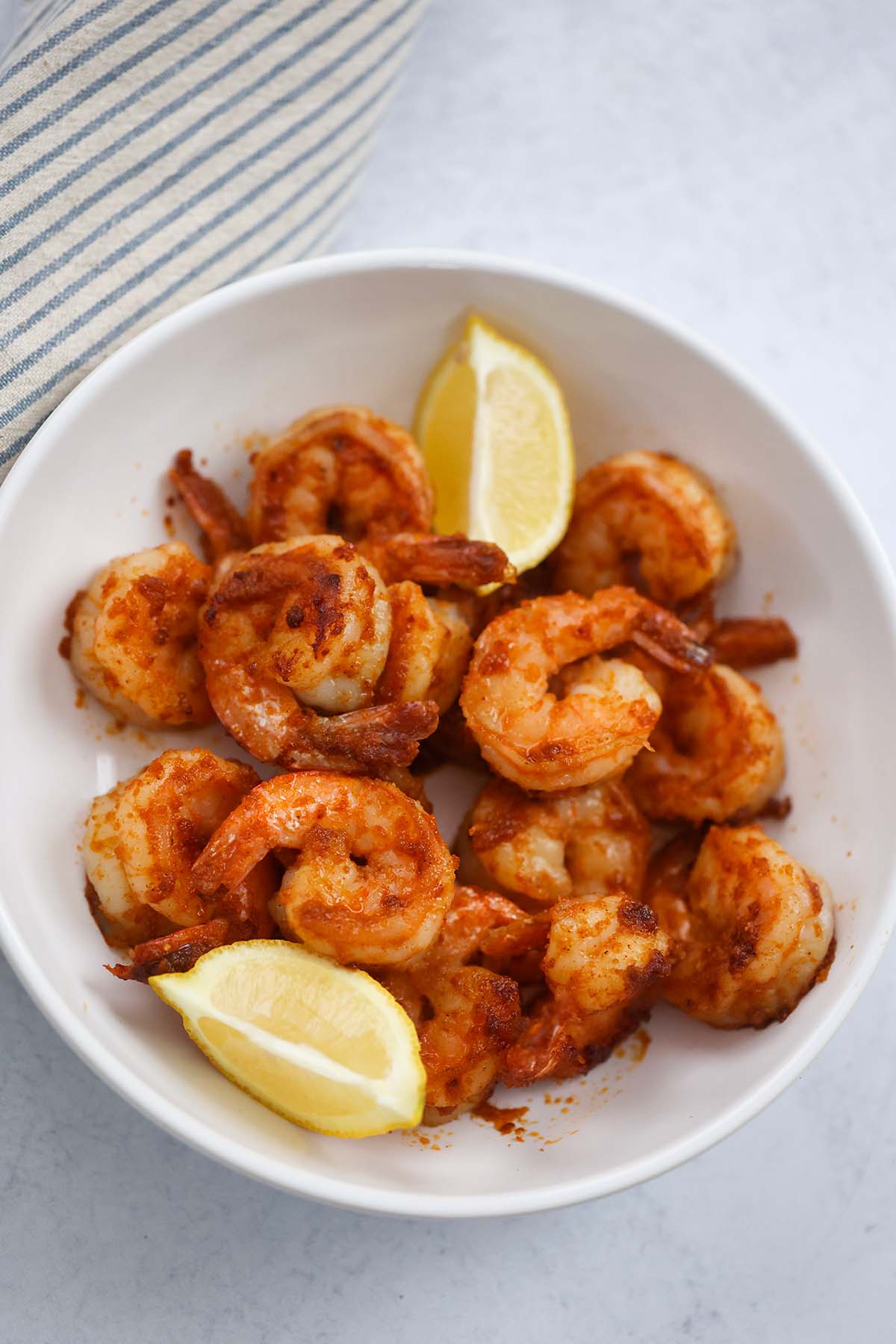 Pan seared shrimp in a bowl with lemon wedges on the side. 