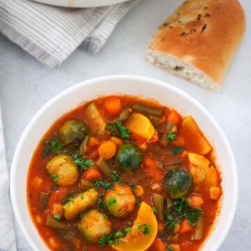 vegetable soup in a bowl with bread on the side.