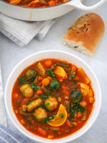 vegetable soup in a bowl with bread on the side.
