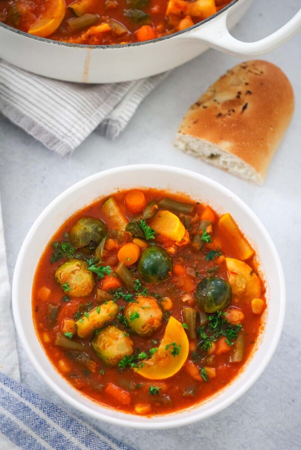 vegetable soup in a bowl with bread on the side.