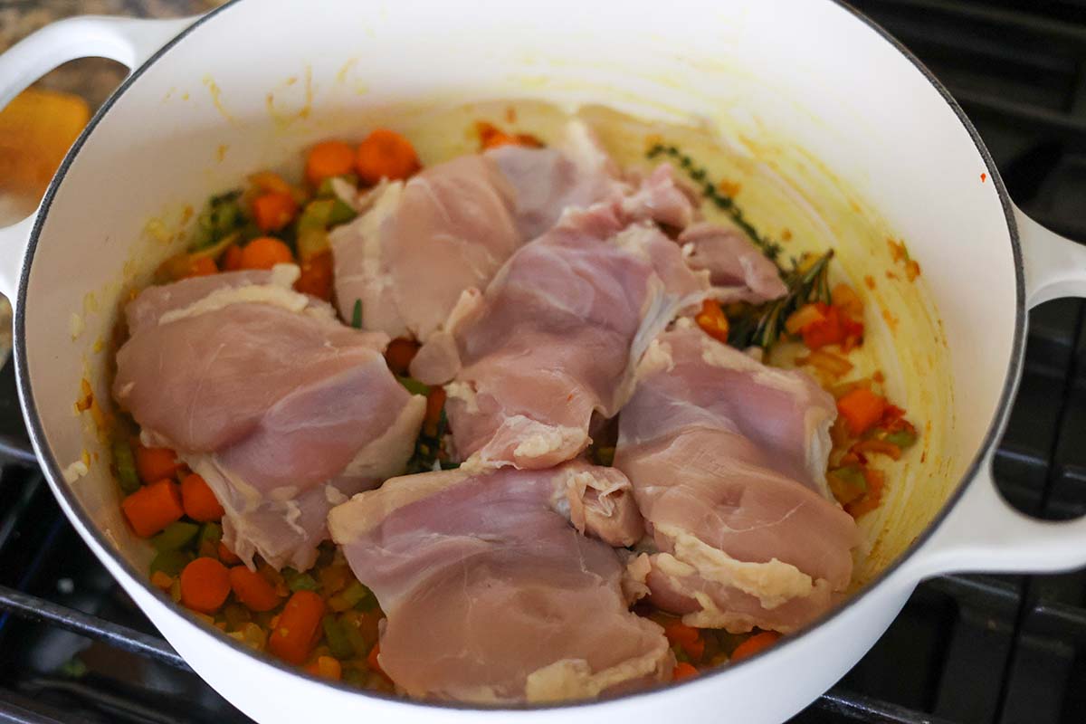 raw chicken, herbs, and veggies in a dutch oven on the stovetop. 
