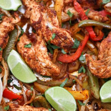 baked chicken tenders, onions, peppers, and lime wedges on a sheet pan.