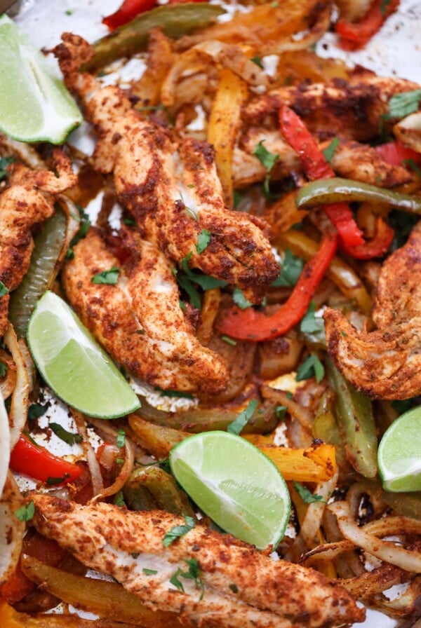 baked chicken tenders, onions, peppers, and lime wedges on a sheet pan.