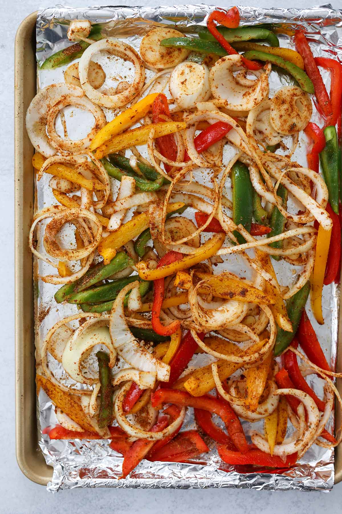 onions and peppers coated in spices on a baking sheet. 