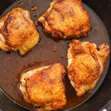 four pan-seared chicken thighs in a cast iron skillet.