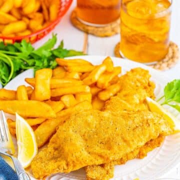 Two Southern fried catfish fillets with fries on a plate and lemon wedges on the side.