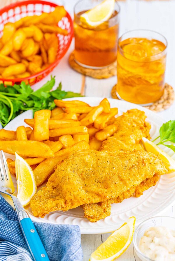 Two Southern fried catfish fillets with fries on a plate and lemon wedges on the side.