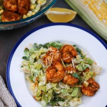 blackened shrimp caesar salad on a plate with a bowl of salad on the side.