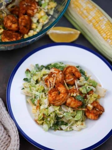 blackened shrimp caesar salad on a plate with a bowl of salad on the side.
