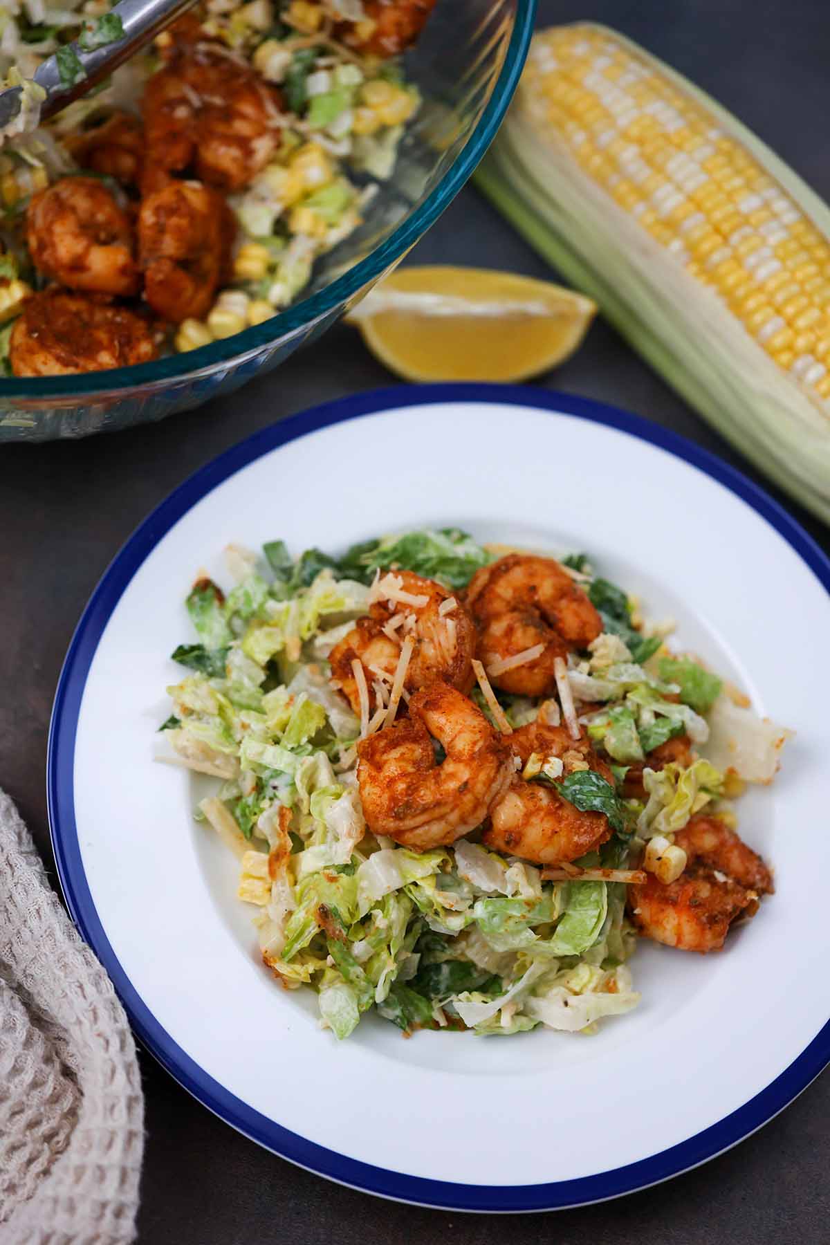 blackened shrimp caesar salad on a plate with a bowl of salad on the side. 
