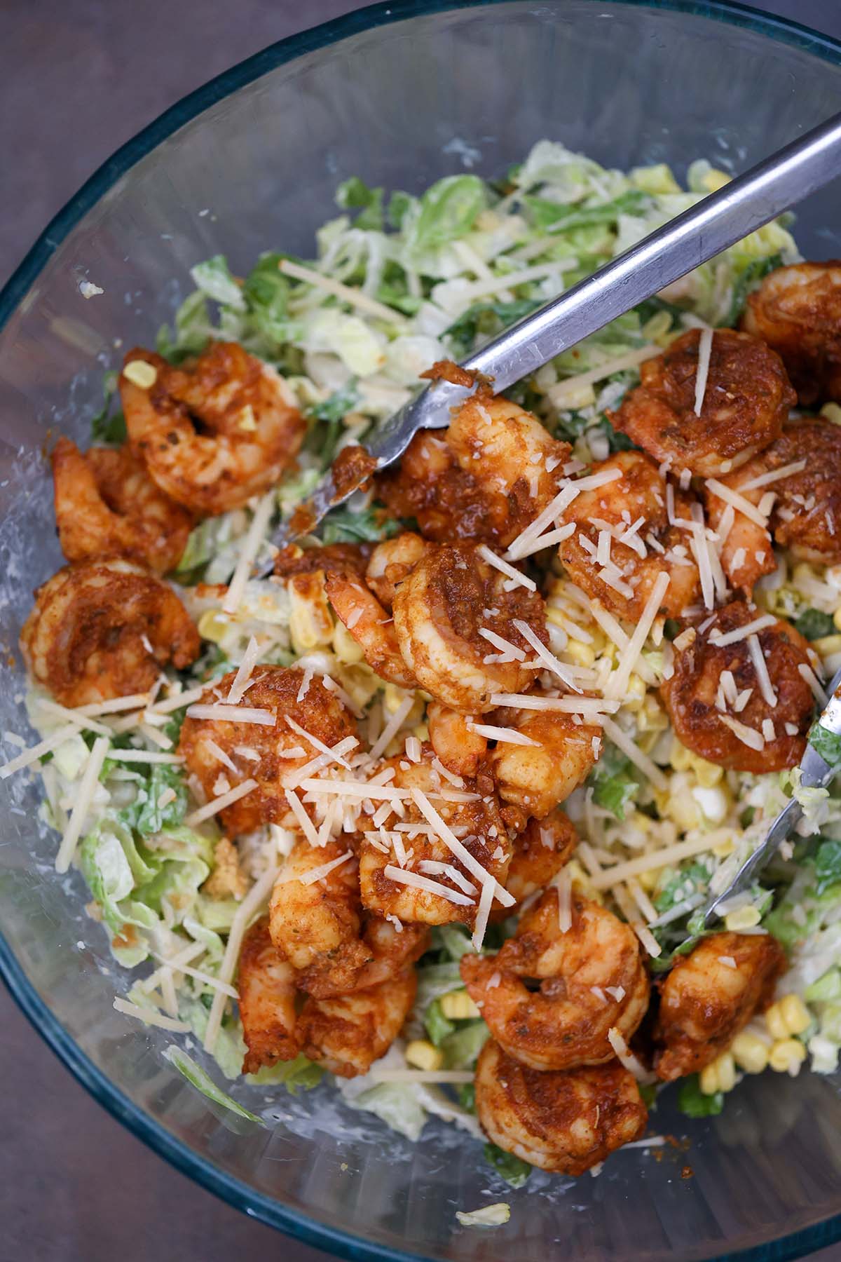 blackened shrimp caesar salad in a bowl with tongs. 