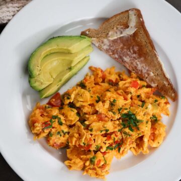 huevos pericos with a slice of toast and sliced avocado on the side.