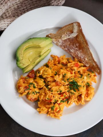 huevos pericos with a slice of toast and sliced avocado on the side.