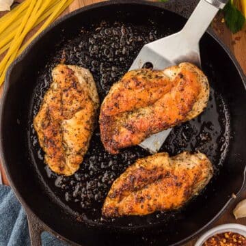 three pan seared chicken breasts in a cast iron skillet.