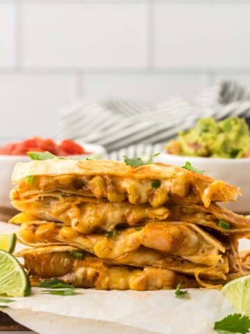 four shrimp quesadillas stacked with limes and guacamole on the side.