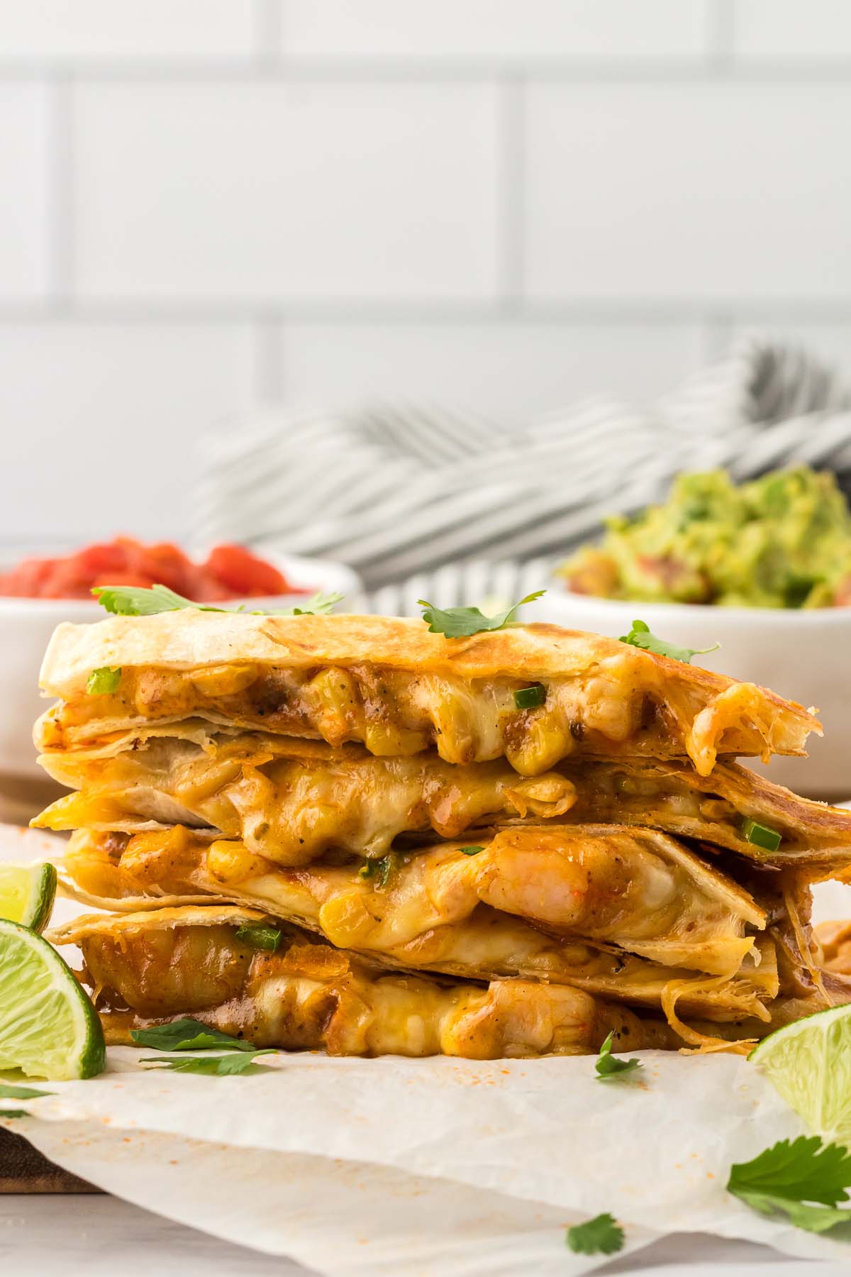 four shrimp quesadillas stacked with limes and guacamole on the side. 