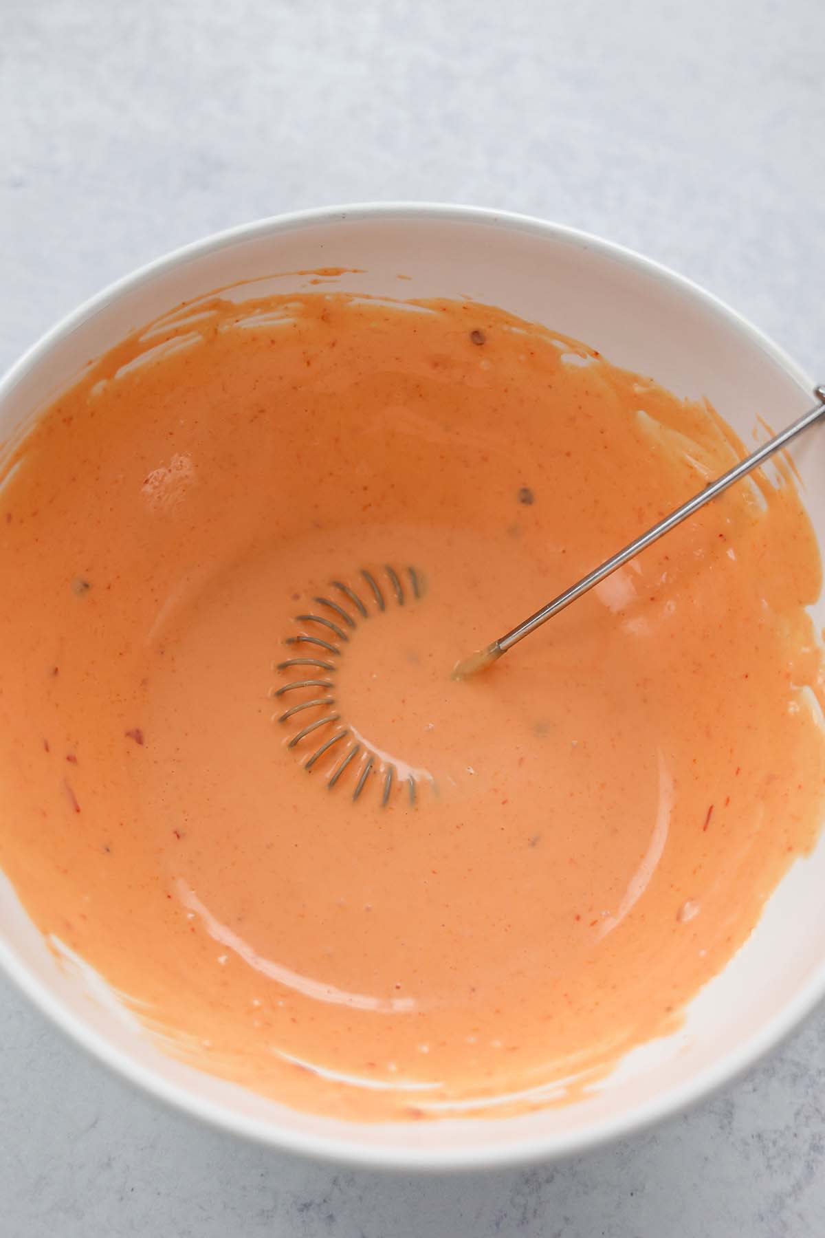 bang bang sauce in a white bowl with a whisk. 
