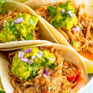 Three shredded chicken tacos with guacamole on top.