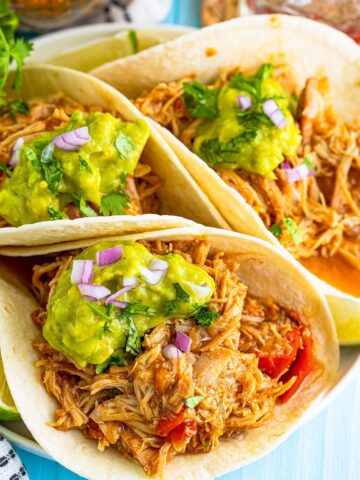 Three shredded chicken tacos with guacamole on top.