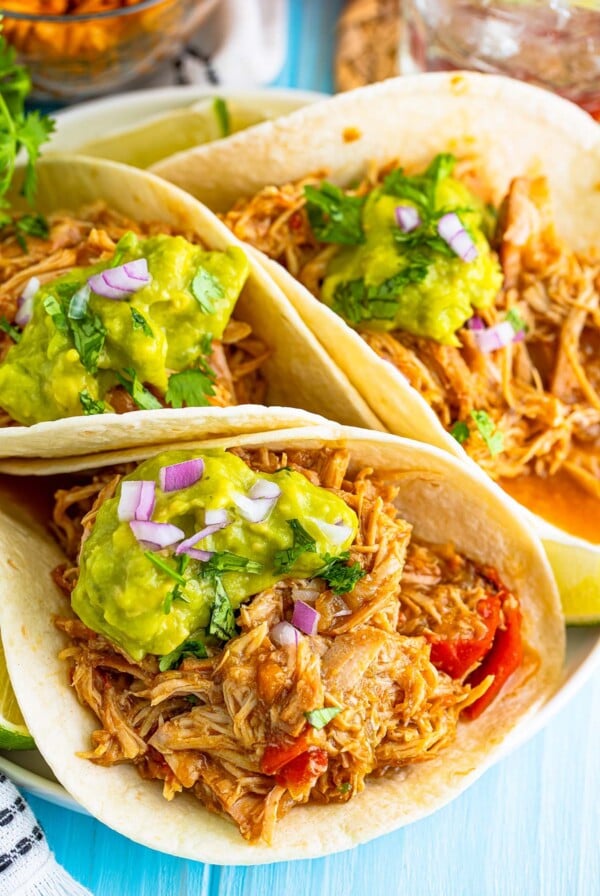 Three shredded chicken tacos with guacamole on top.