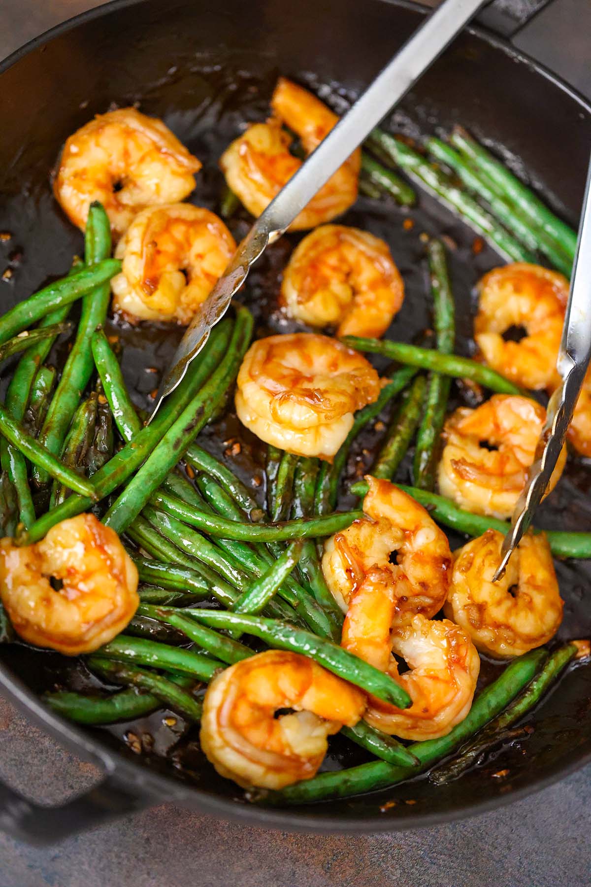 honey shrimp and green beans in a black skillet with tongs. 