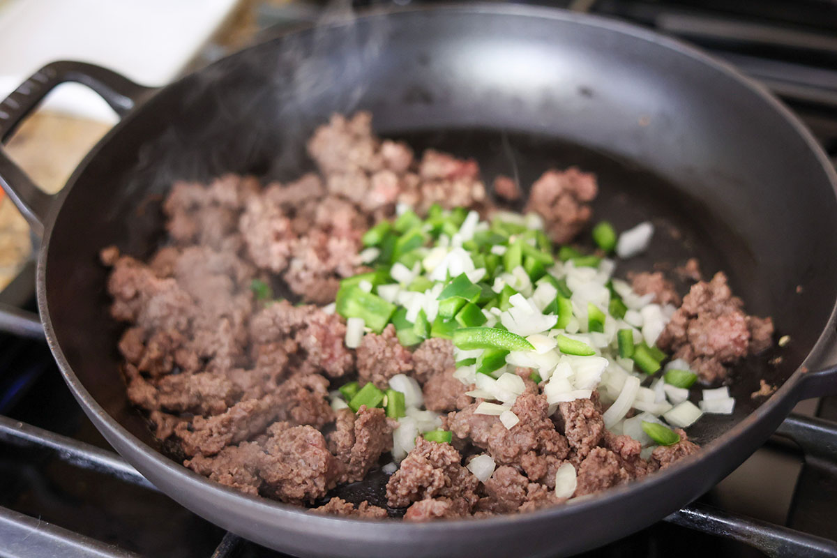 ground beef cooking in a skillet with onions and peppers. 