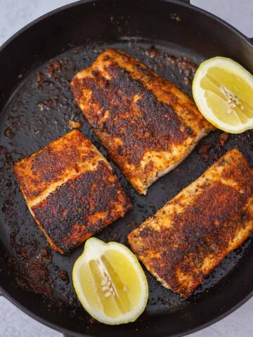 three blackened mahi mahi fillets with lemon wedges on the side.