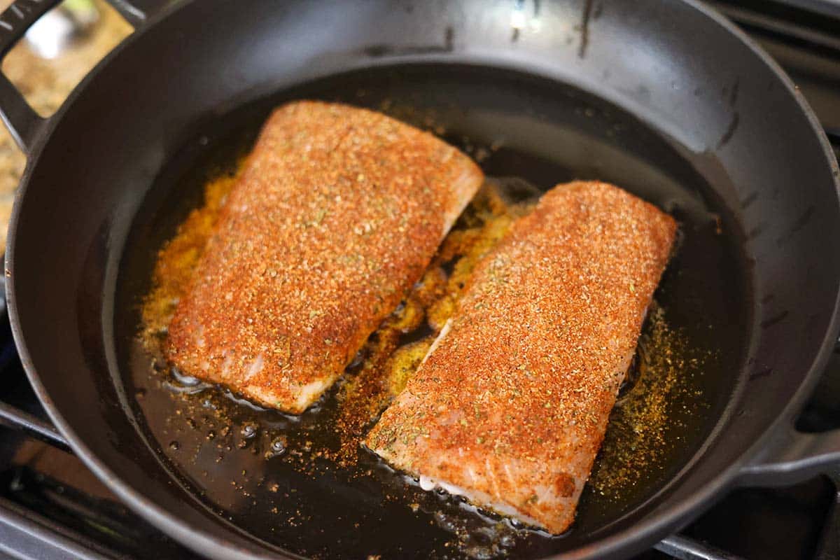 two mahi mahi fish fillets cooking in a skillet on the stovetop. 